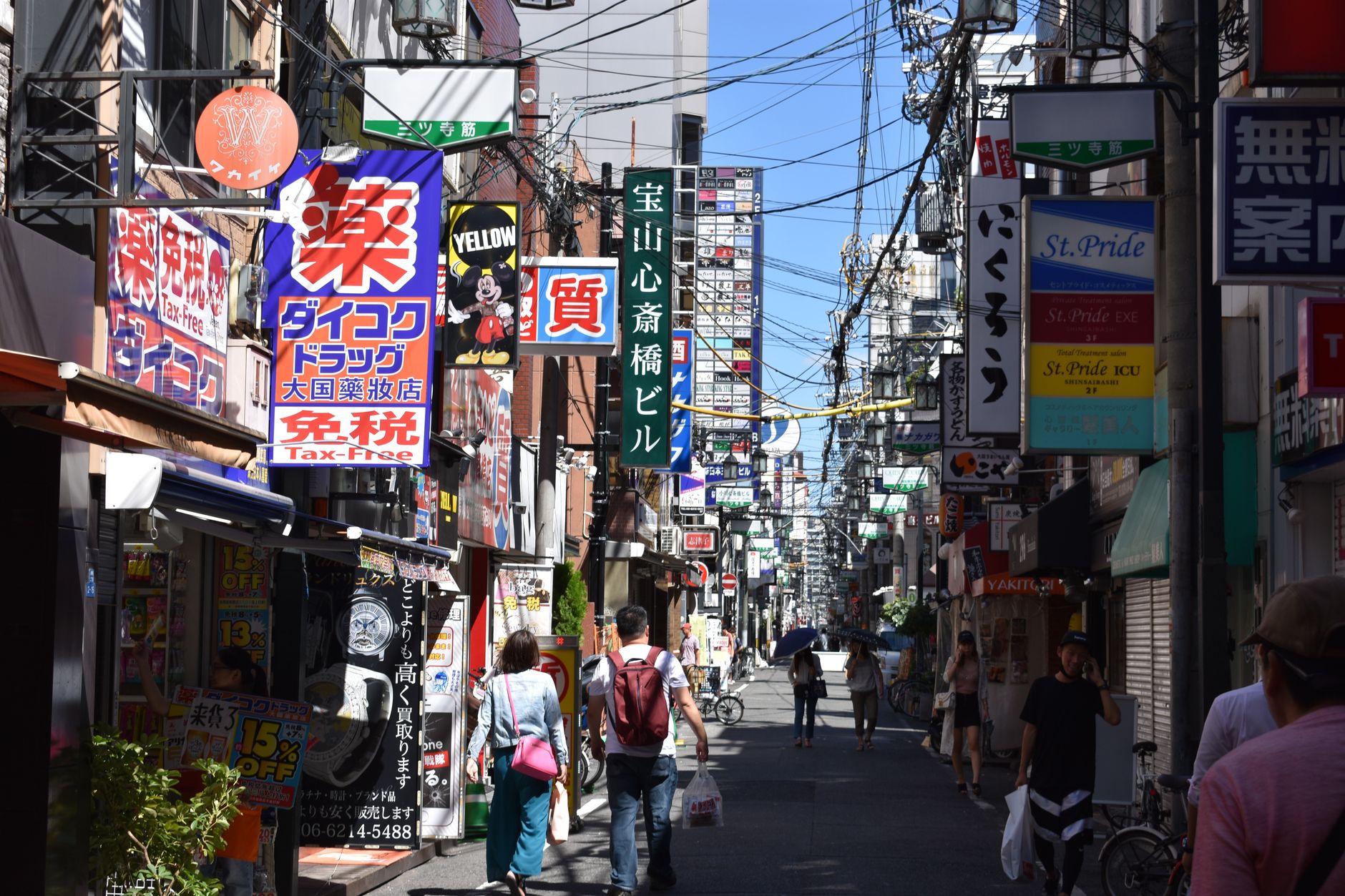 Bustling urban street in Osaka with colorful advertisements and pedestrians in daylight. — 9 seater car hire for team travel