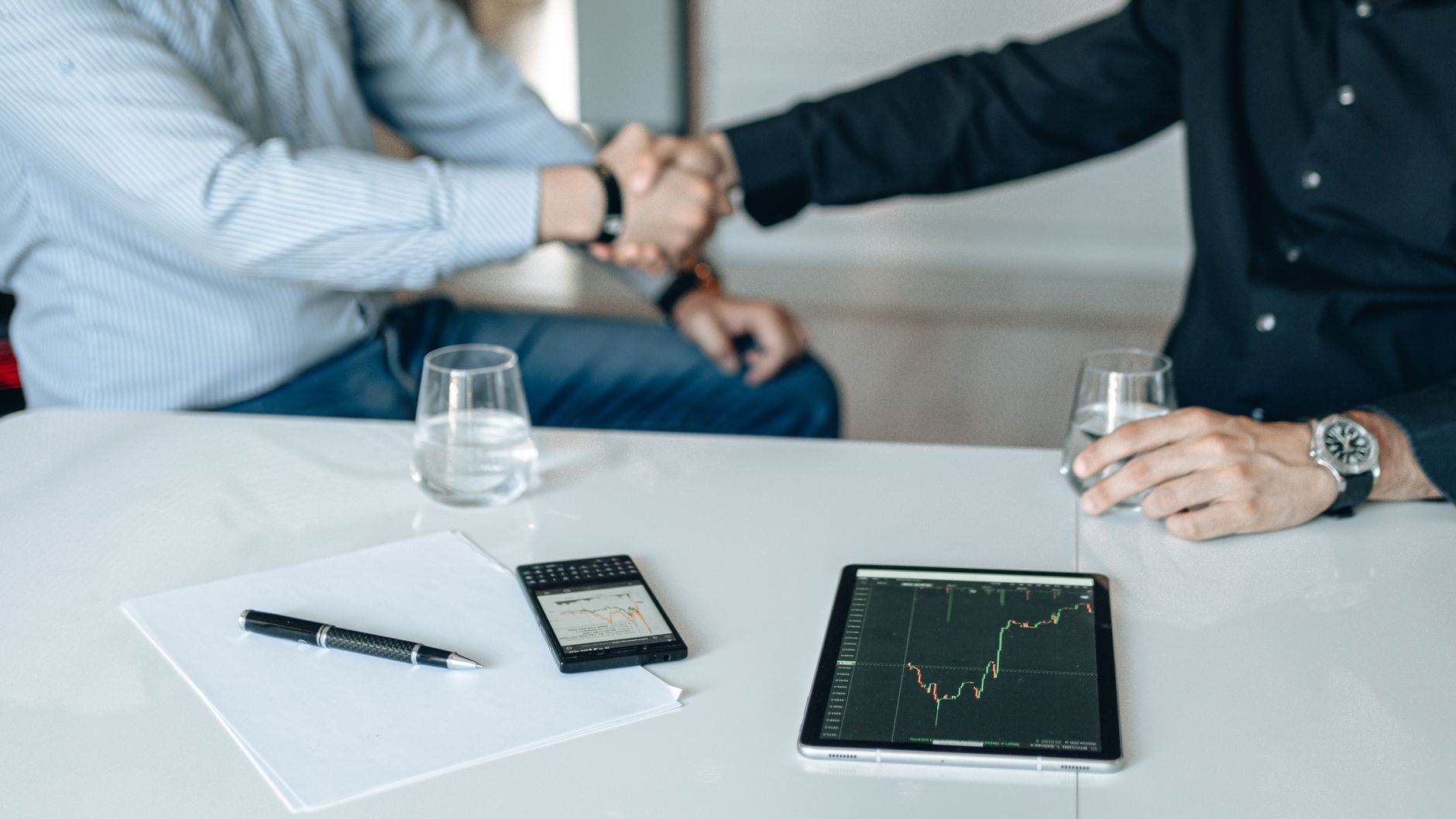 Business meeting with handshake and financial analysis displayed on a tablet. — Top Agencies Achieve SEO Excellence with Agen